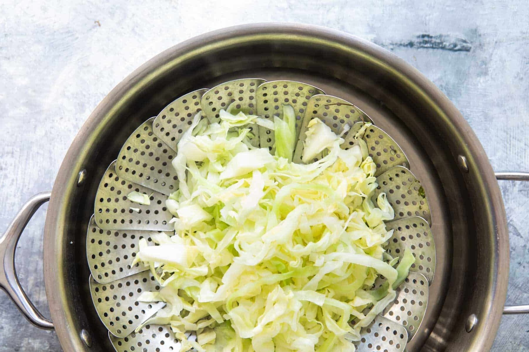 Cabbage being steamed in a steamer basket in a silver pan.