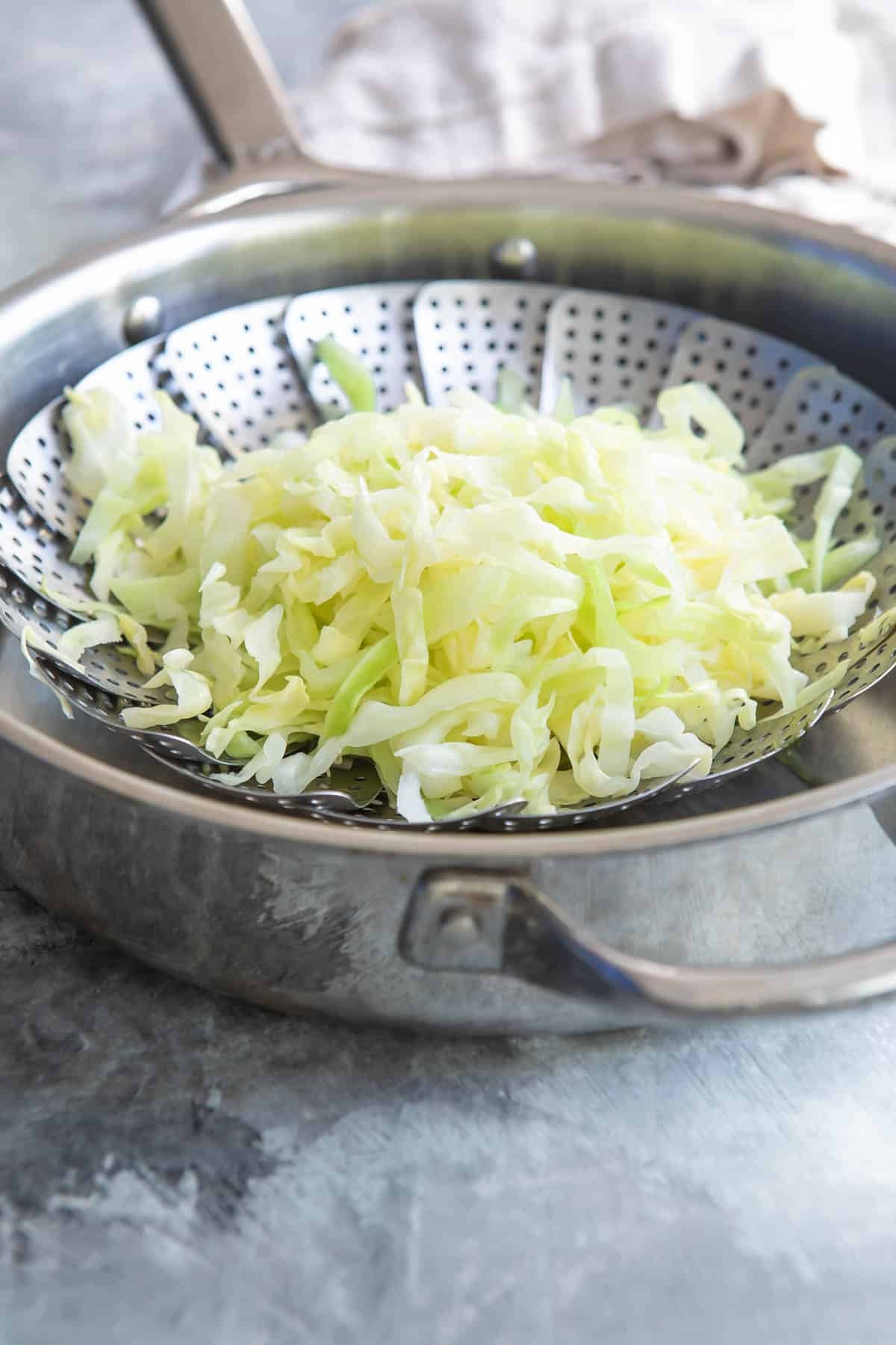 Cabbage being steamed in a steamer basket in a silver pan.