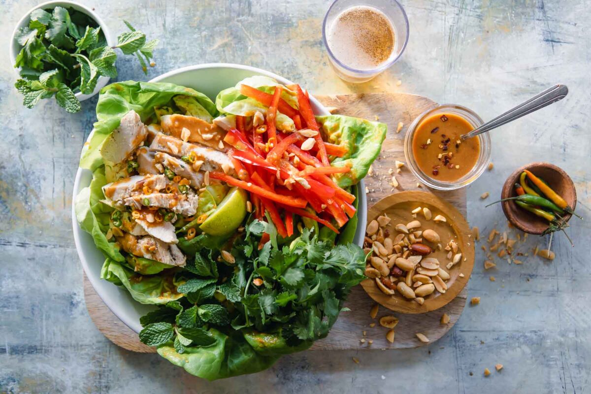 A Thai chicken salad on a plate with a small jar of dressing next to it.