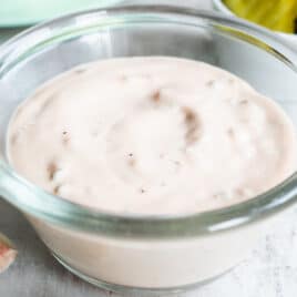 Thousand Island dressing in a clear bowl on a countertop with pickles and lettuce in the background.