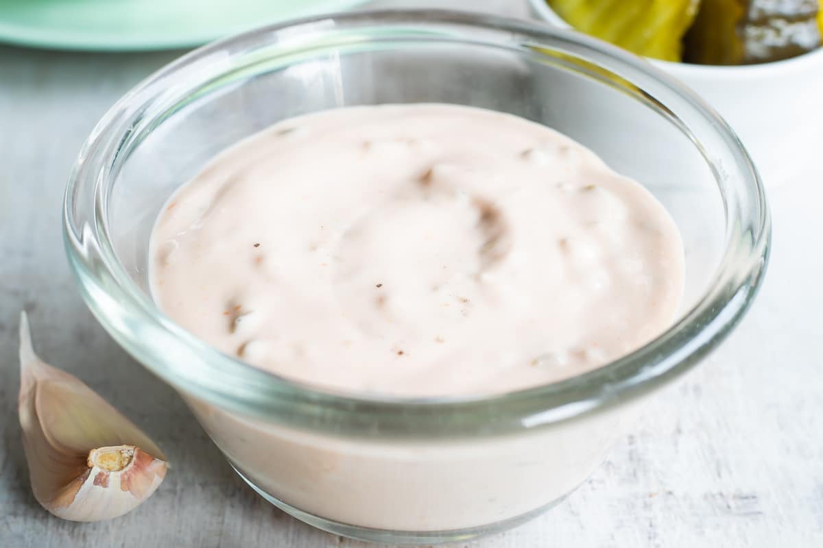Thousand Island dressing in a clear bowl on a countertop with pickles and lettuce in the background.