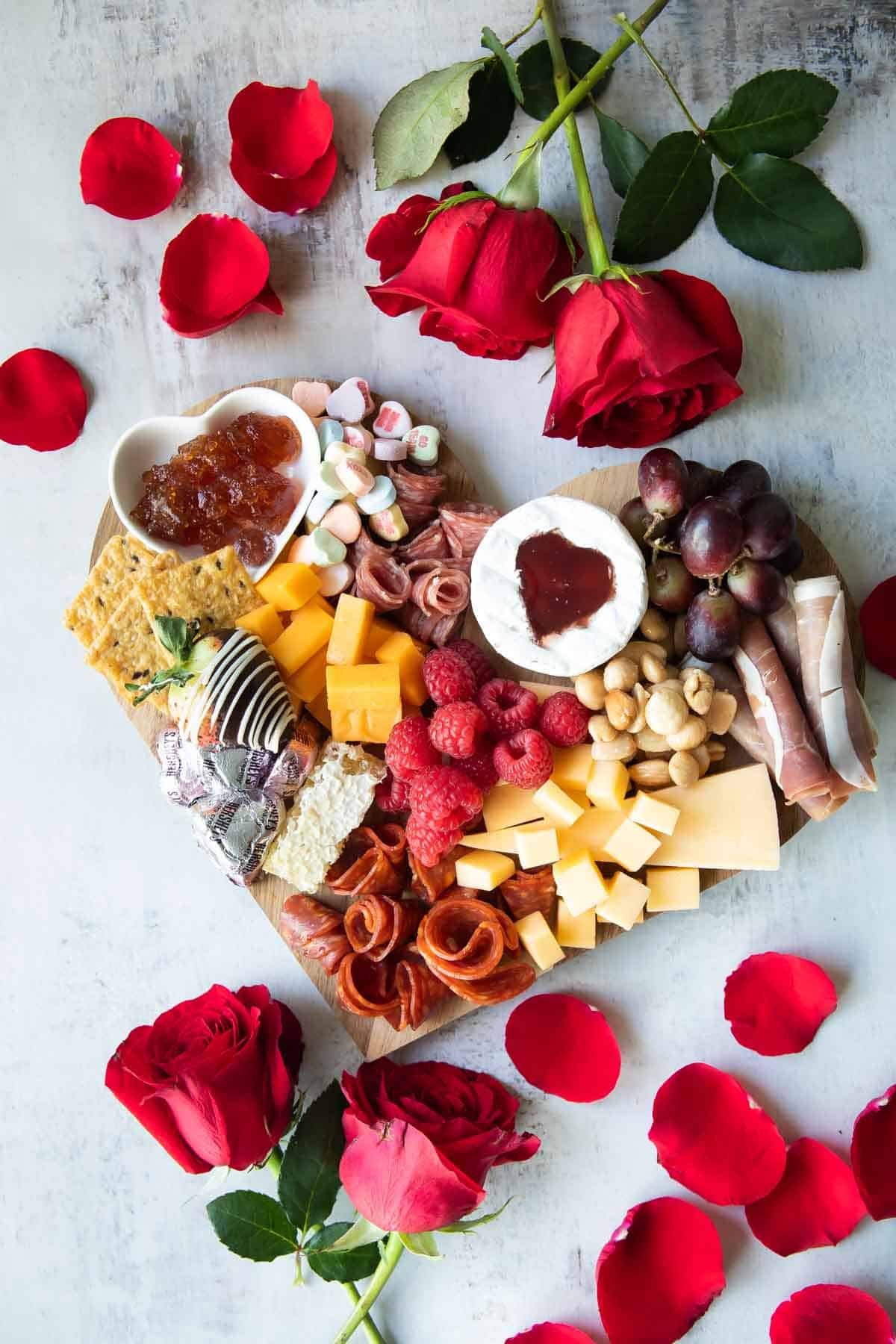 A fully-built Valentine's Day charcuterie board with roses around it.