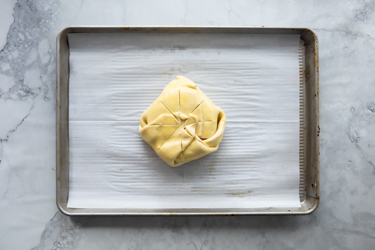 Wrapping a wheel of brie with apricot ja on top in puff pastry, slits cut in the pastry.