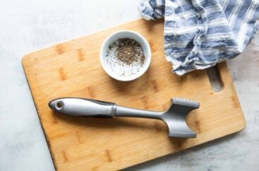 An OXO meat tenderizer on a cutting board next to a bowl of salt and pepper.