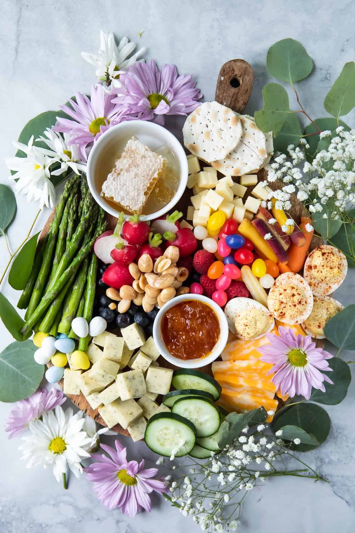 An Easter charcuterie board filled with cheese, spreads, veggies, fruit, and flowers.