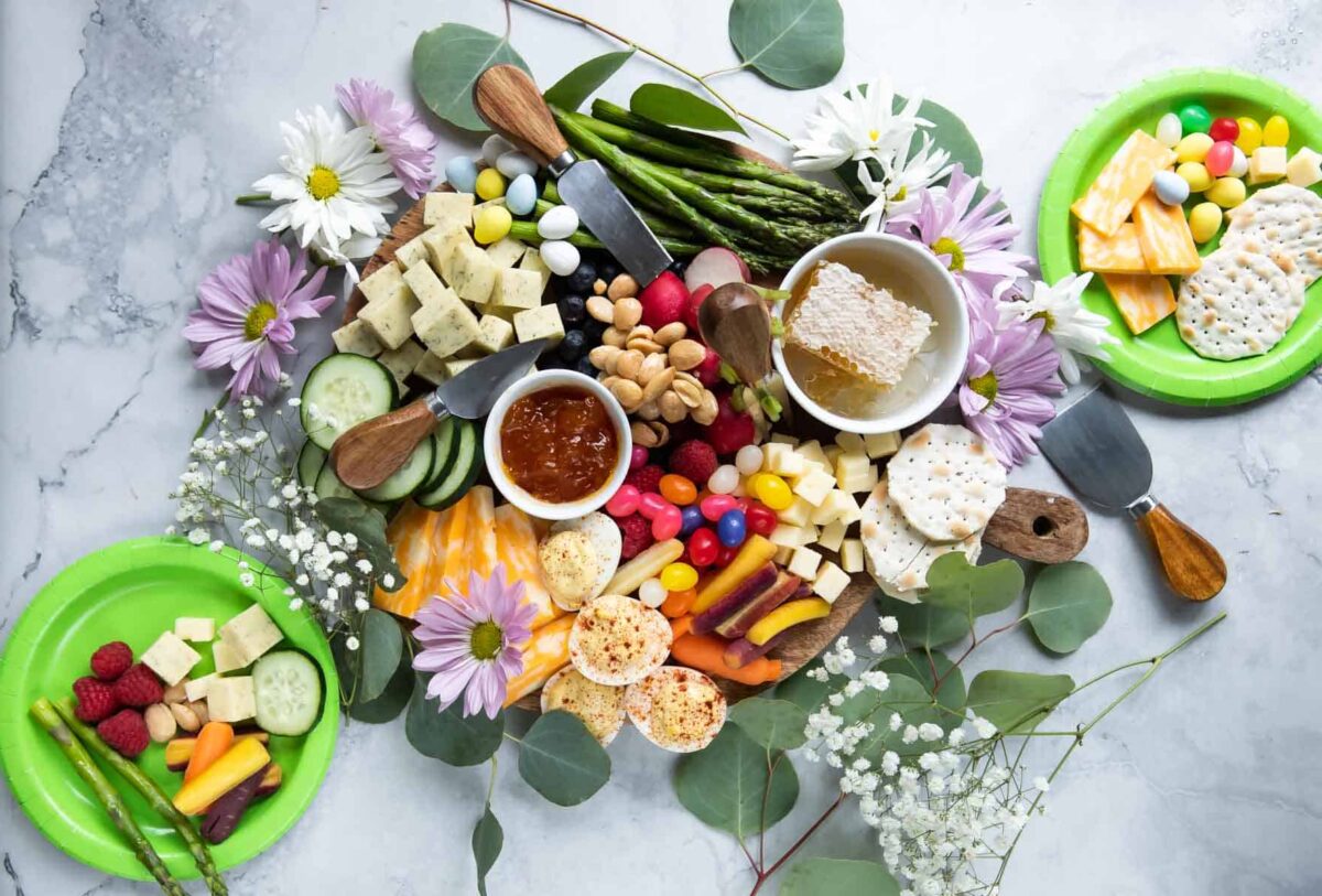 An Easter charcuterie board filled with cheese, spreads, veggies, fruit, and flowers.