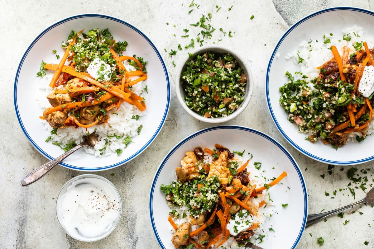 Three white plates of Harissa chicken and rice.