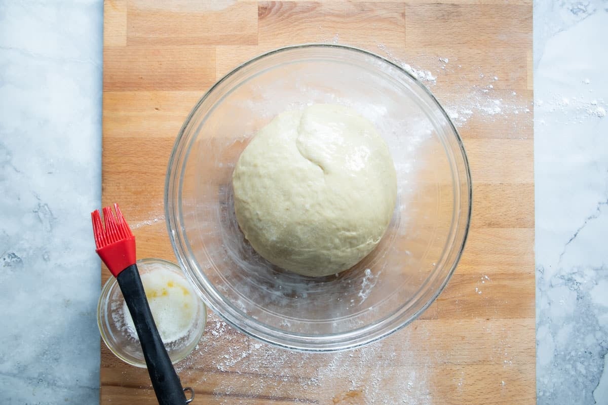 A ball of dough brushed with butter in a glass dish.