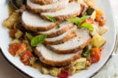 An overhead shot of pork loin with ratatouille on a white platter.