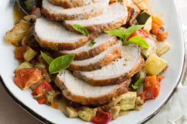 An overhead shot of pork loin with ratatouille on a white platter.