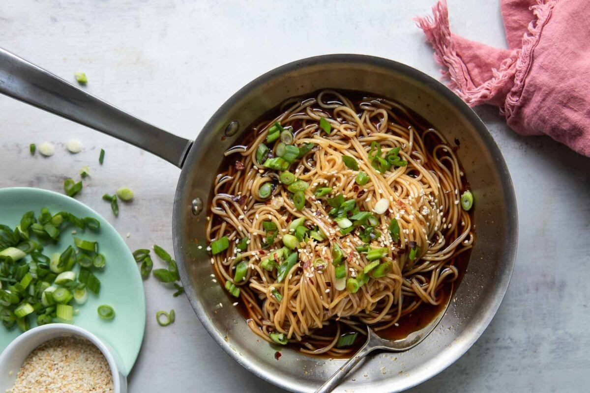 A skillet of teriyaki noodles garnished with scallions.