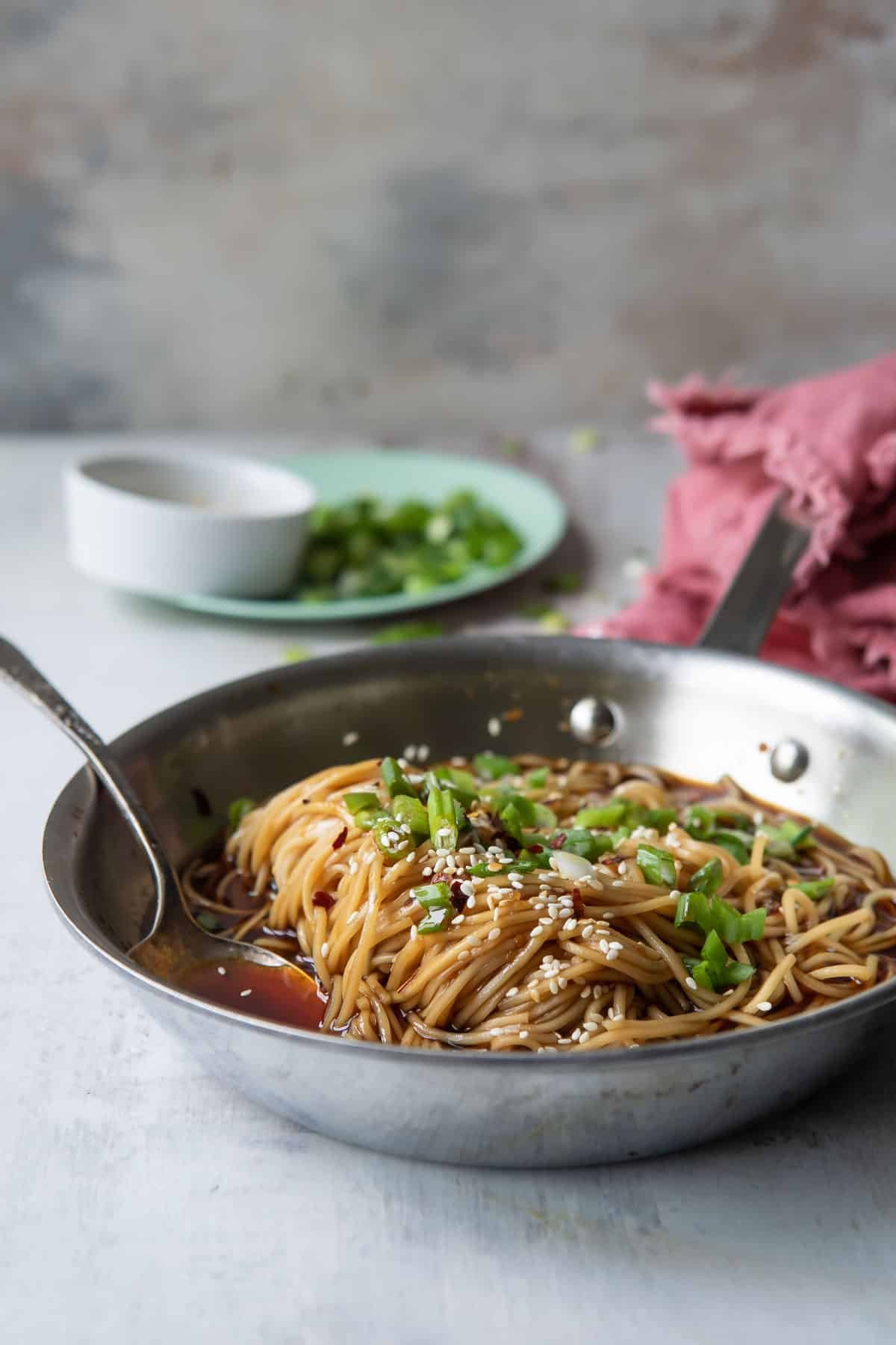 A skillet of teriyaki noodles garnished with scallions.