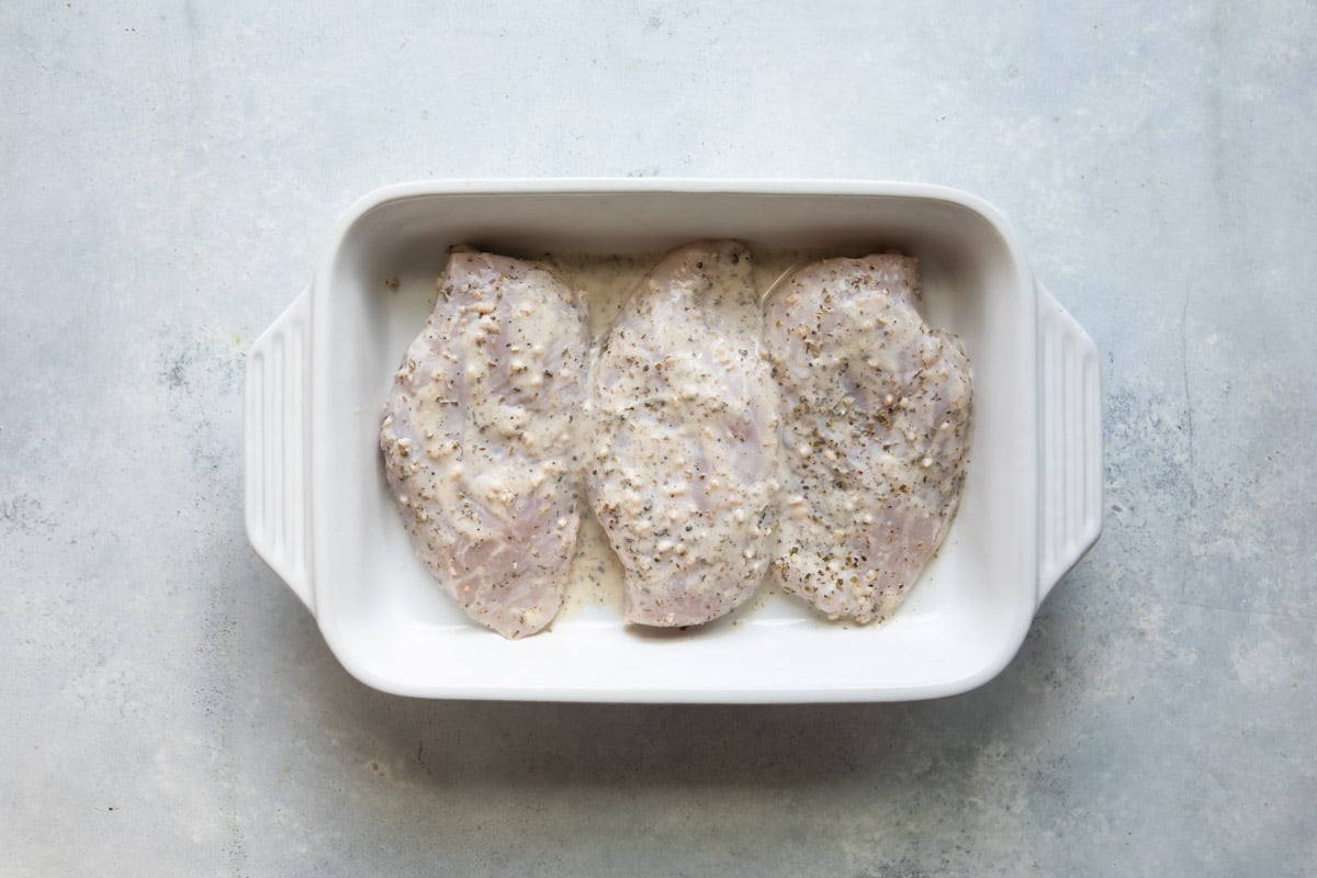 Raw Greek chicken in a baking dish.