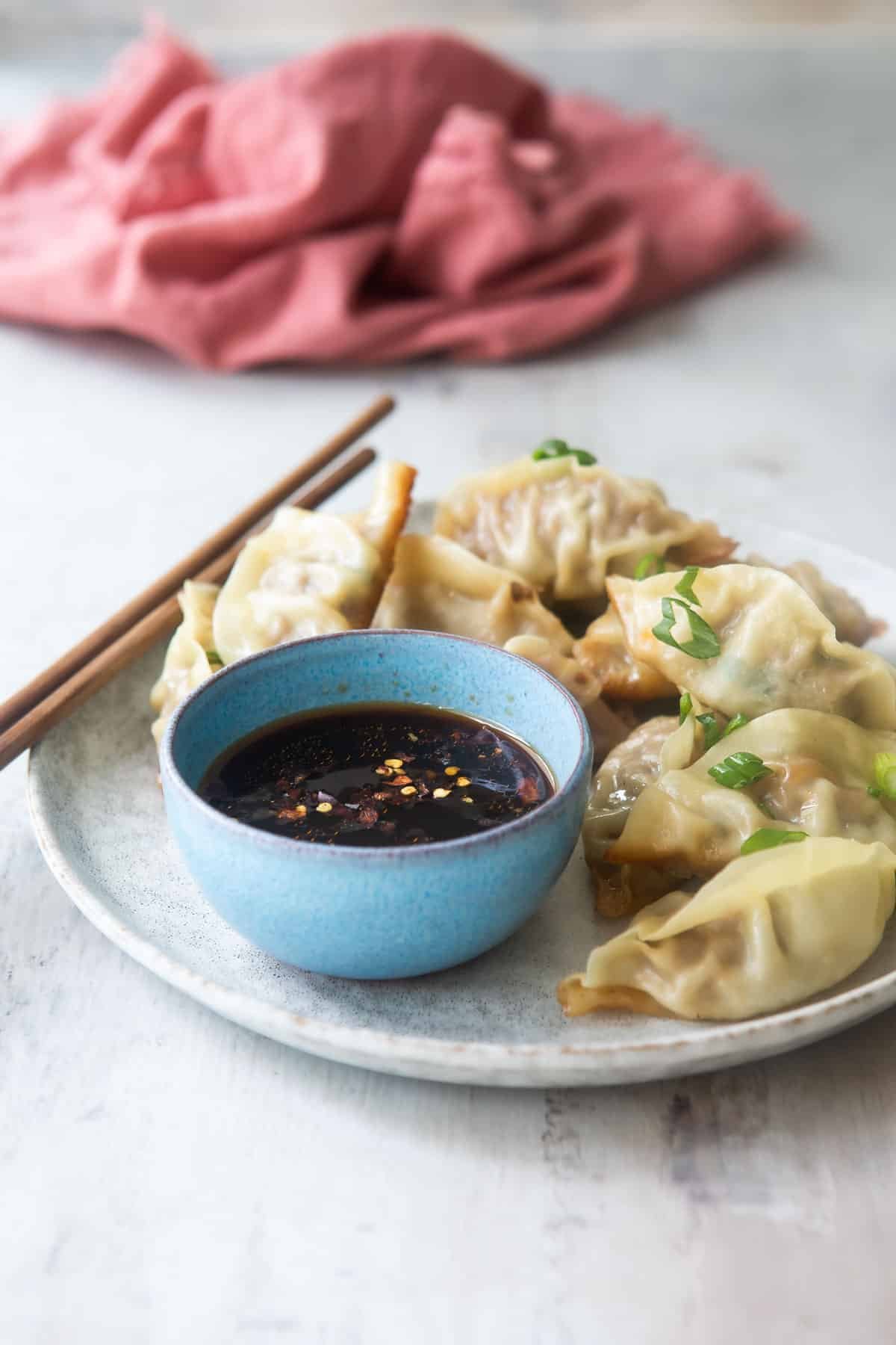 A platter of potstickers, someone holding one with chopsticks.