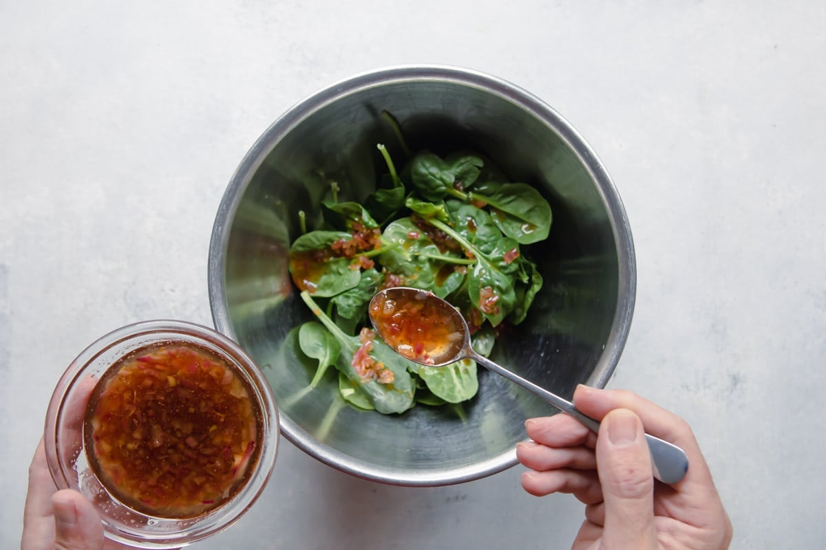 Dressing spinach leaves with bacon dressing.