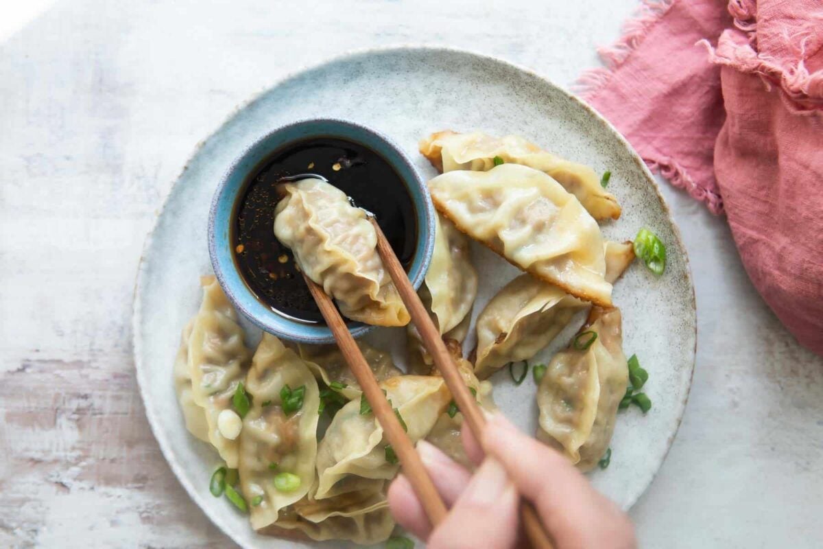 A platter of potstickers, someone holding one with chopsticks.