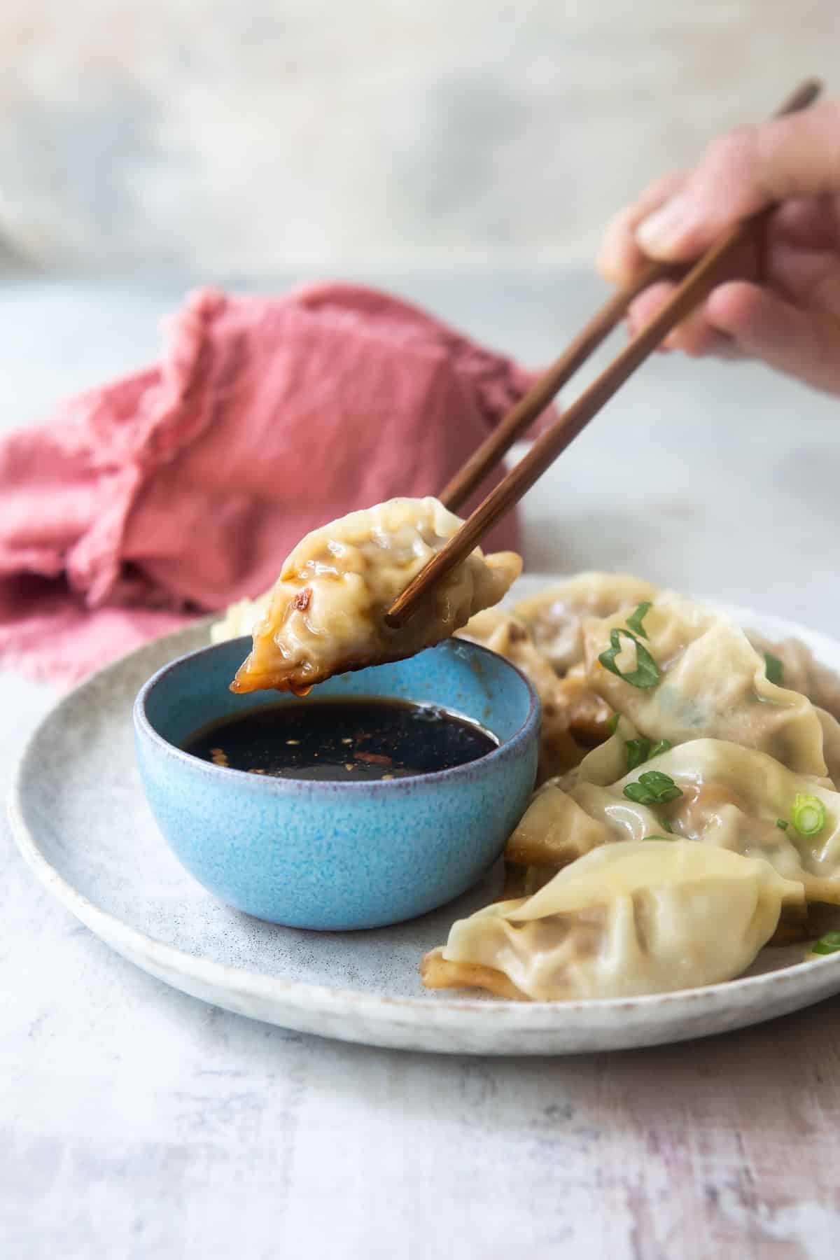 A platter of potstickers, someone holding one with chopsticks.