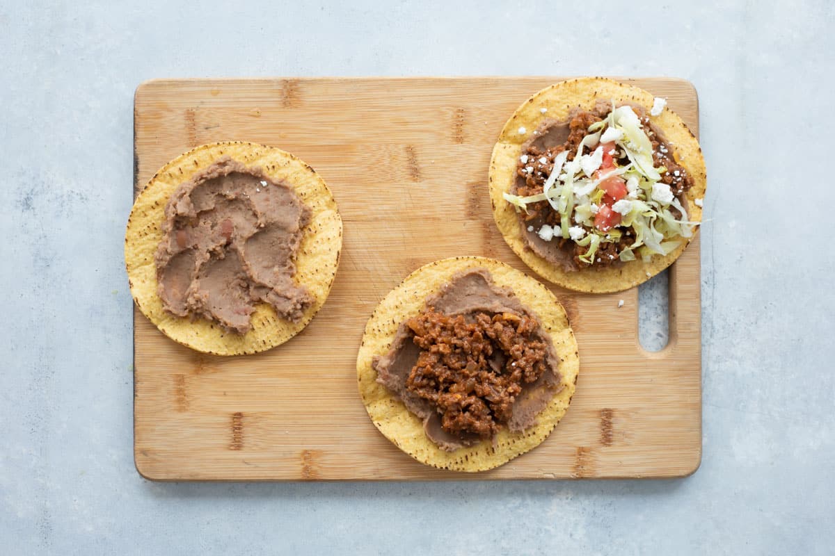 Assembling tostadas on a wooden cutting board.