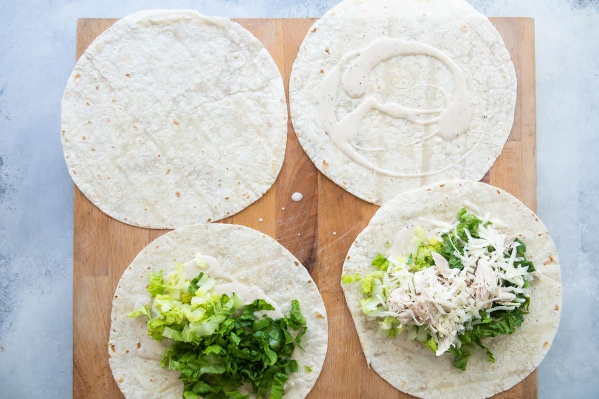 Assembling chicken caesar wraps on a board.