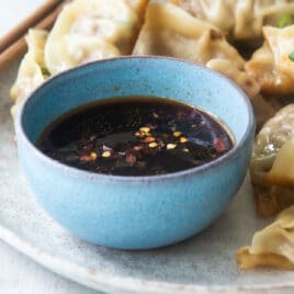 A platter of potstickers, someone holding one with chopsticks.
