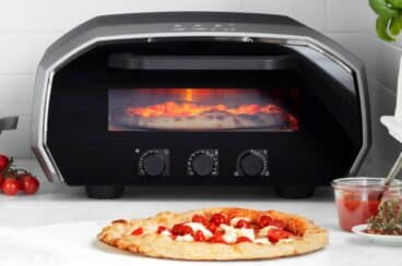 An ooni pizza oven with a pizza in front of it.