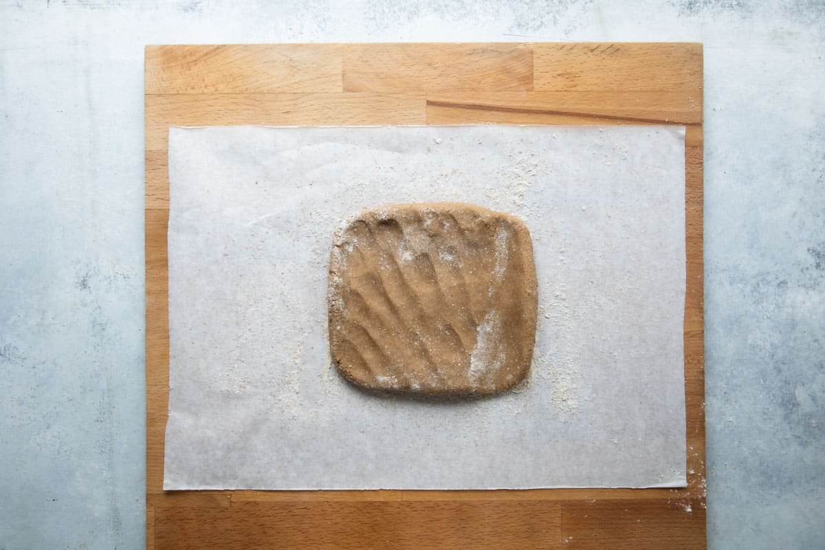 A square of graham cracker dough on parchment to be rolled out.