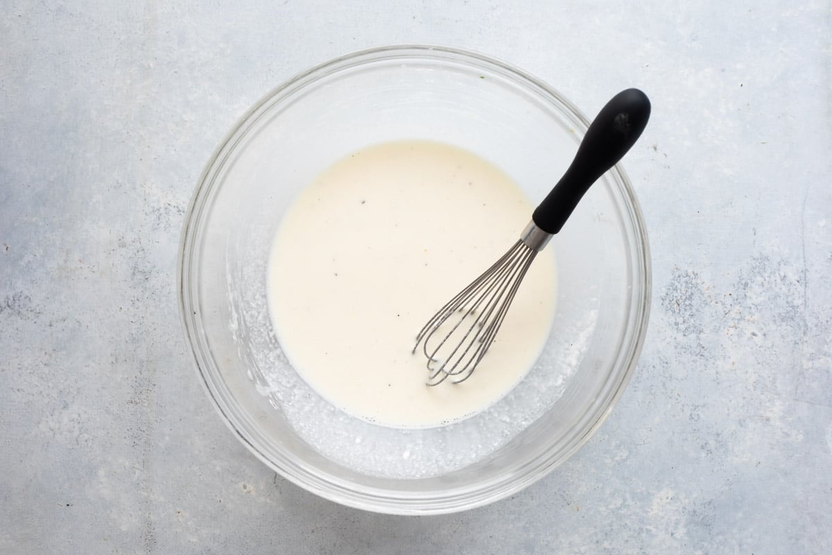 Coleslaw dressing in a clear bowl with a whisk.