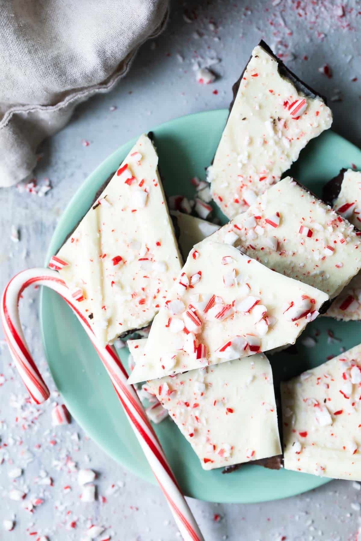 Peppermint bark and a candy cane on a teal plate.