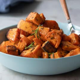 A bowl of roasted sweet potoates with a spoon resting in it.