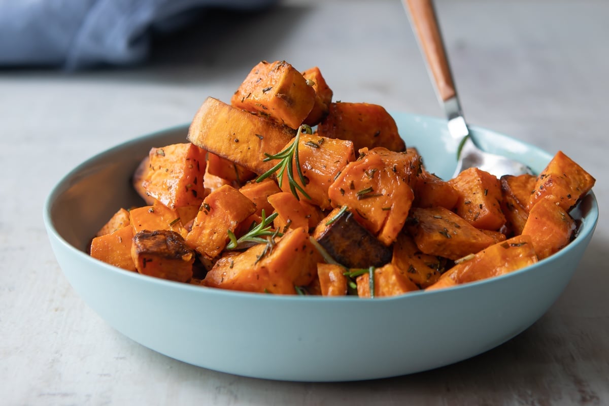 A bowl of roasted sweet potoates with a spoon resting in it.