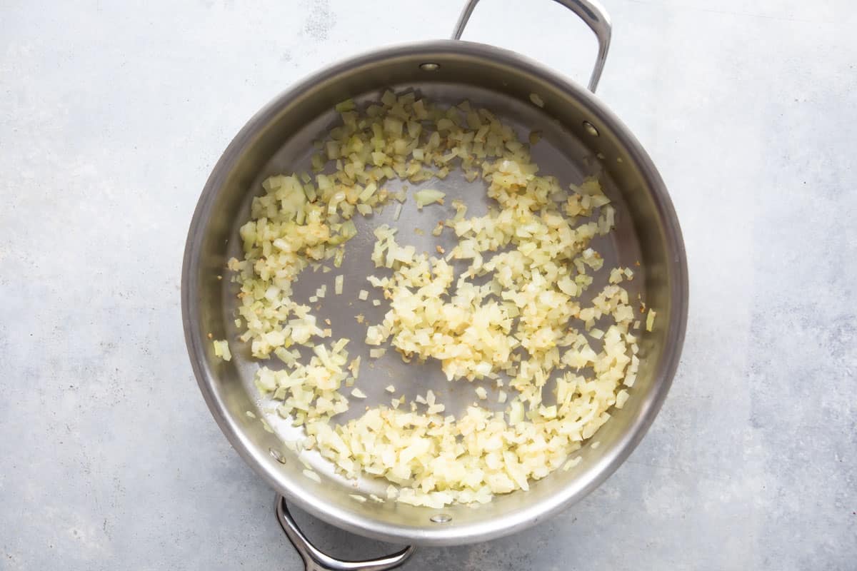 Onion for chicken lettuce wraps being cooked in a silver pan .