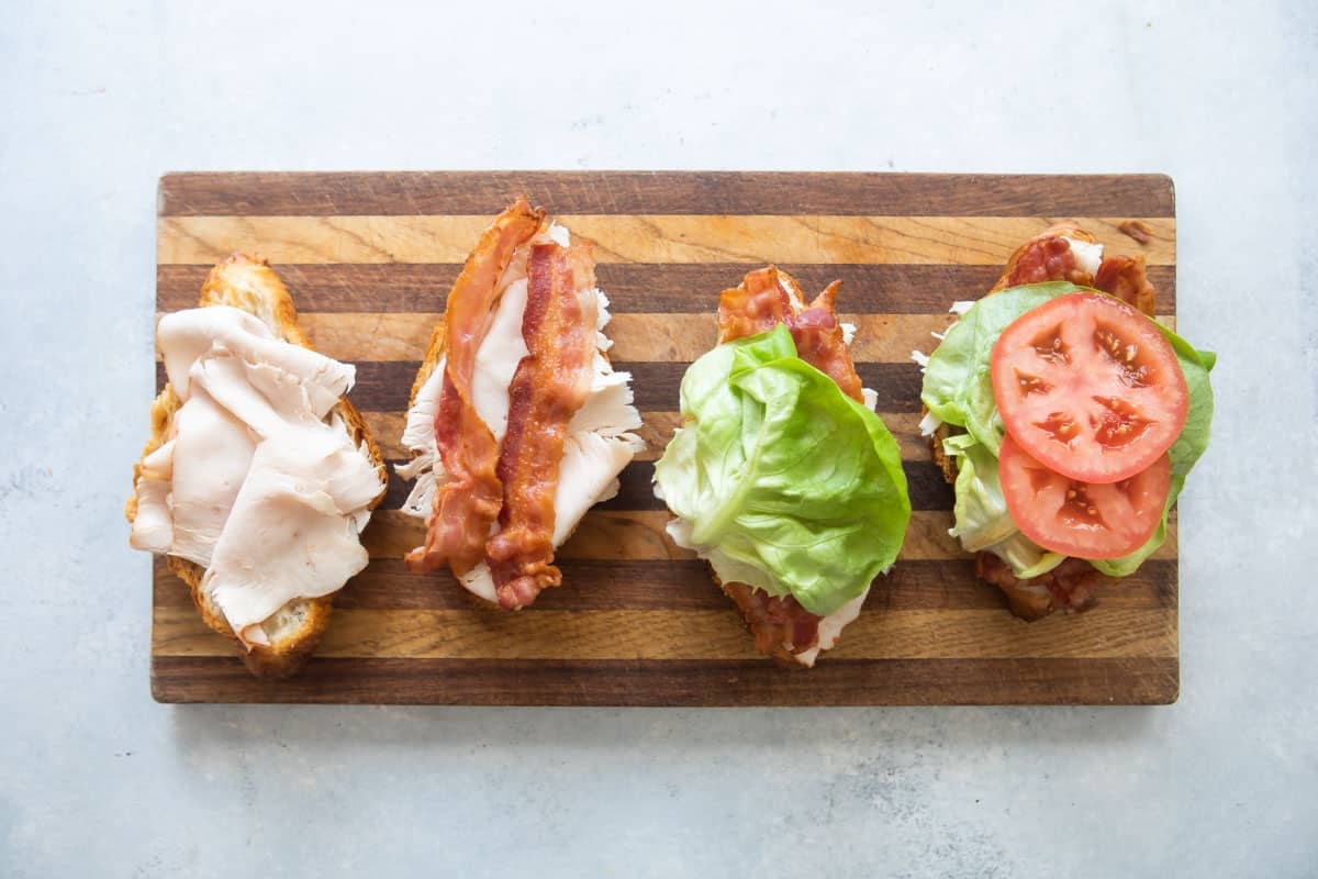 Croissant sandwiches being assembled on a wooden cutting board.