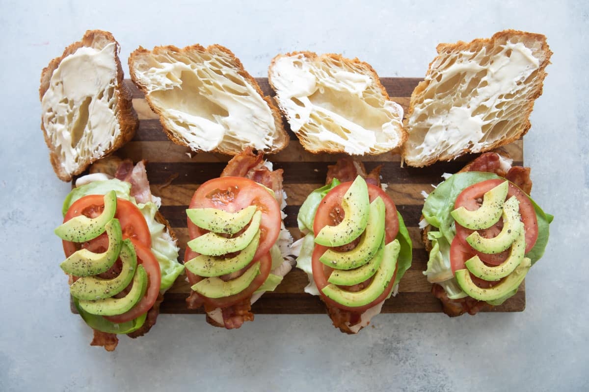 Croissant sandwiches being assembled on a wooden cutting board.