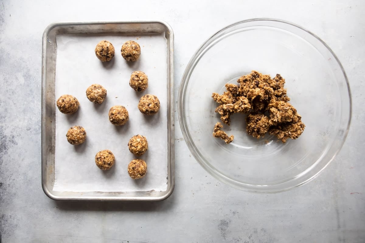 Energy balls rolled out next to a bowl of their ingredients.