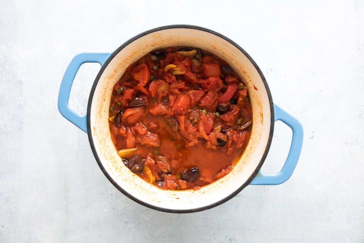 A Dutch oven with sauce ingredients for pasta puttanesca.