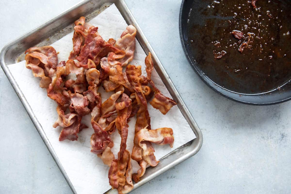 Bacon resting on a paper towel lined baking sheet after being fried.