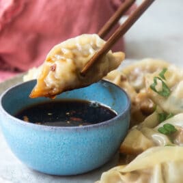 A platter of potstickers, someone holding one with chopsticks.