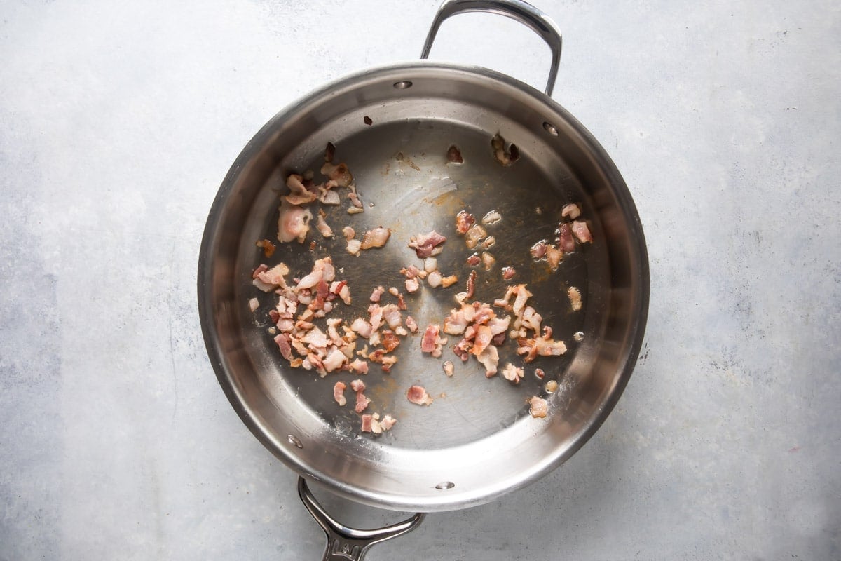 Bacon being cooked in a silver skillet.
