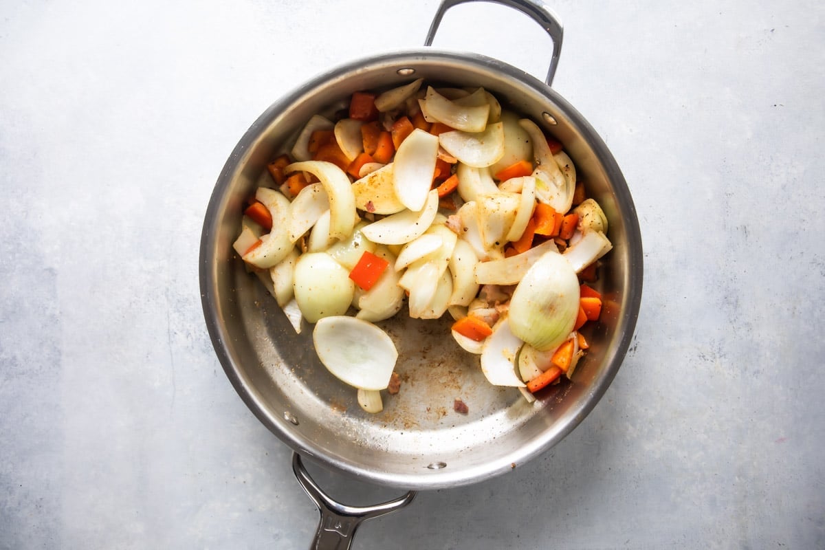 Onion, pepper and spices being cooked in a silver skillet.