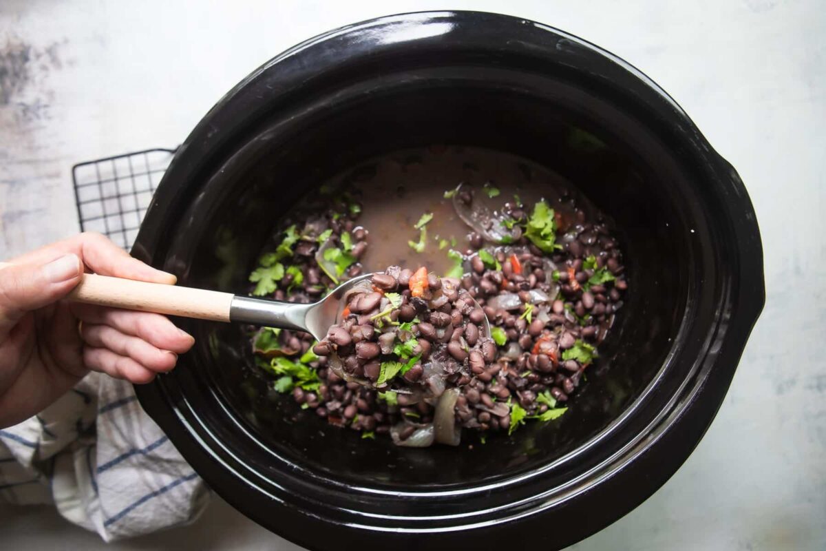 Slow cooker black beans being scooped out of a slow cooker.