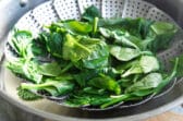 A steamer basket filled with steamed spinach.