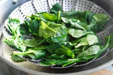 A steamer basket filled with steamed spinach.