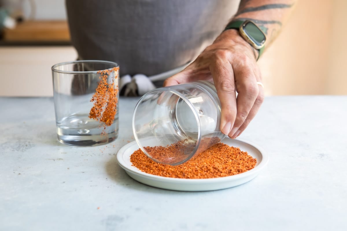 Someone rolling a glass in Tajin for a strawberry paloma.