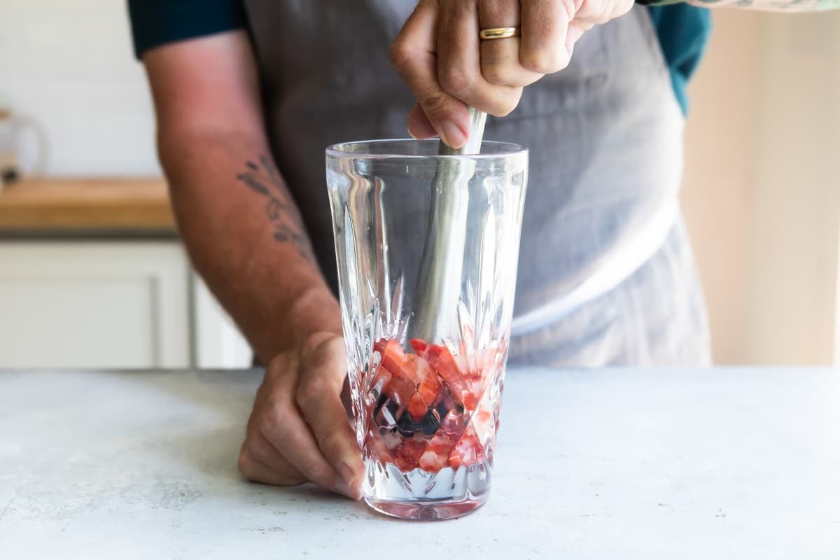 Someone muddling ingredients for a strawberry paloma in a glass.
