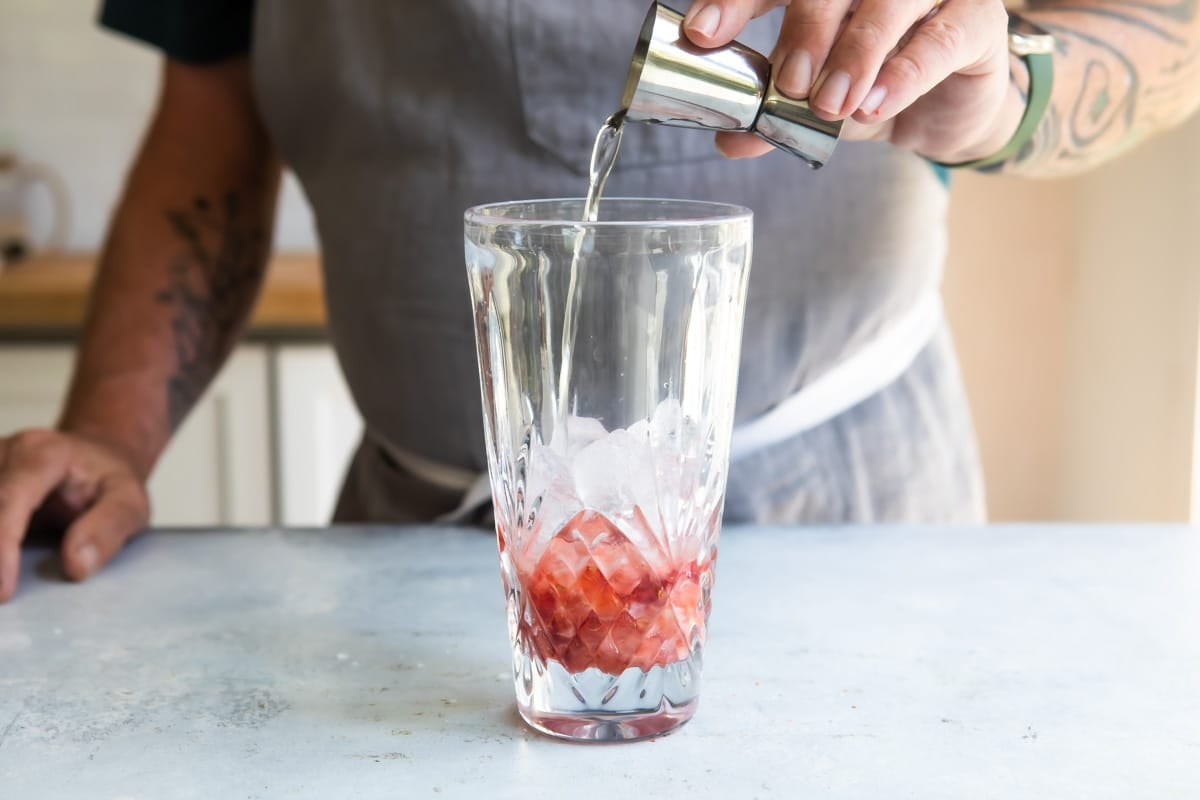 Someone pouring tequila into a glass to make a strawberry paloma.