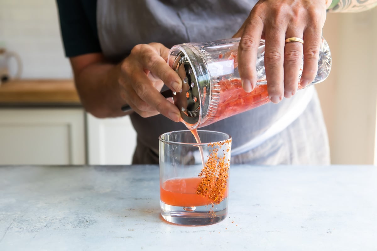 Someone pouring a strawberry paloma into a glass.