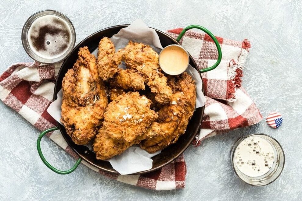 Fried chicken on a platter next to a beer and coleslaw.