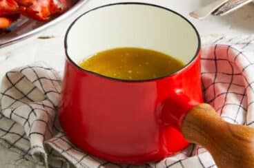 A red butter warmer with a wooden handle.