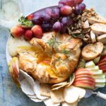 A platter with fruits, crackers and nuts with baked brie in puff pastry in the middle.