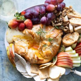 A platter with fruits, crackers and nuts with baked brie in puff pastry in the middle.